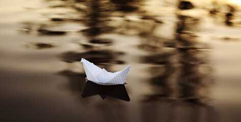 A paper boat is floating on the waves in the water at a beautiful sunset. Origami ship Sailing. The...