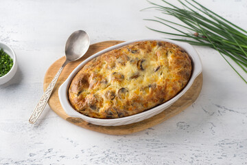 Casserole or clafoutis with mushrooms and cheese in a white ceramic baking dish sprinkled with green onions on a light background