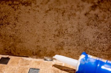 Silicone caulk being applied along a tile joint in a bathroom shower.