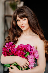 an attractive woman with long hair and bare shoulders and a bouquet of peonies