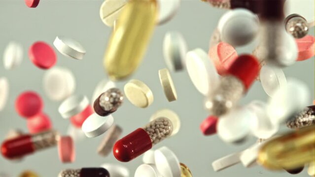 Various medical pills and capsules take off and slowly rotate in flight. On a gray background. Filmed is slow motion 1000 fps.