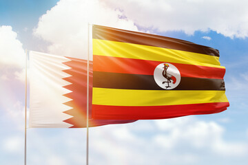 Sunny blue sky and flags of uganda and qatar