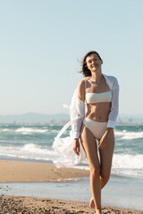 Fototapeta na wymiar happy young woman in white shirt and swimwear walking on sea shore.