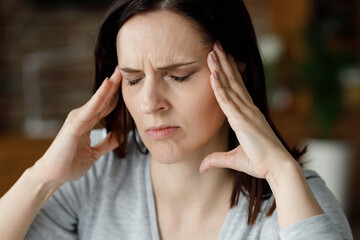 Upset young woman suffering from headache. Exhausted woman with closed eyes massaging the temples...