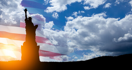 Statue of Liberty with a large american flag and blue sky on background.