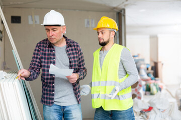 Foreman counting building materials and checking amount with list. Confused builder standing near his boss.