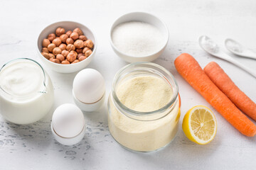 Ingredients for sweet carrot semolina pie or mannik with nuts: semolina, natural yogurt, carrots, hazelnuts, eggs, lemon, sugar, salt, baking powder on a light blue background