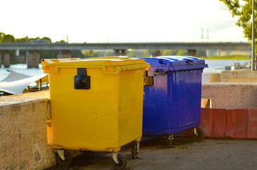Yellow and blue garbage bin stand on the embankment in the city.