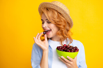 Picking eating cherry fruit. Charming woman with cherry plate isolated on yellow.
