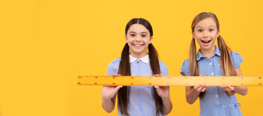 Obraz premium School girls friends. Happy schoolchildren hold wooden ruler. Geometry lesson. School education. Portrait of schoolgirl student, studio banner header. School child face, copyspace.
