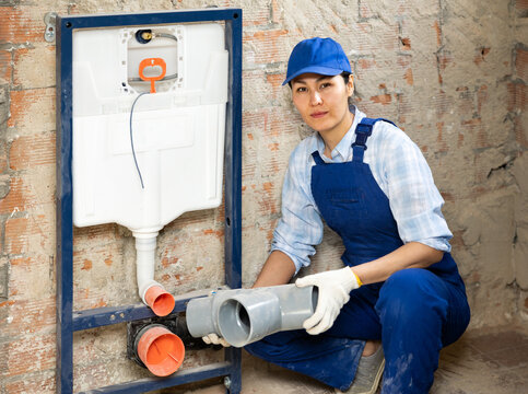 Portrait of focused female professional plumber holding waste pipe connector near mounted on wall cistern and waste pipes for back to wall toilet