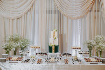 Candy bar. A white wedding cake is adorned with flowers on the banquet table with lots of hors d'oeuvres on the side. Wedding. Side view, top.