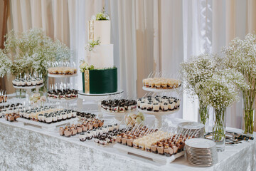 Candy bar. A white wedding cake is adorned with flowers on the banquet table with lots of hors d'oeuvres on the side. Wedding. Side view, top.