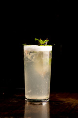 refreshing long drink with foam, mint on wooden table on black background front view