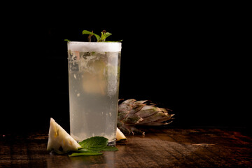 refreshing long drink with foam, pineapple, mint on wooden table on black background