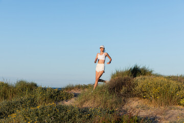 young sportive woman in baseball cap and wireless earphones running on beach.