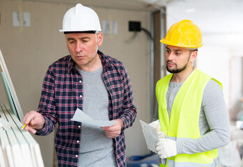 Focused adult civil engineer holding list of tasks and giving instructions to young bearded foreman...