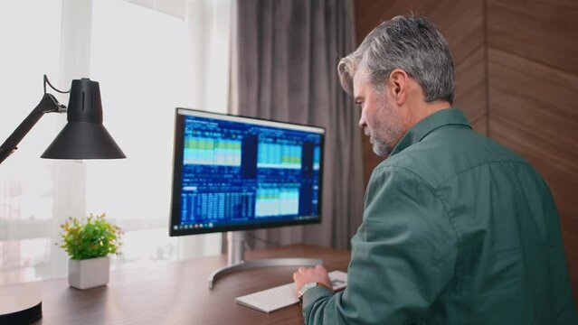 Trader analysing trading charts on stock market in office. Back view on middle-aged male in shirt looking at the screen with stock graphs.