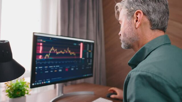 Side view close up portrait of middle-agged broker typing and looking on the sceen. Graphs analysis, stock market. 4k. Office atmosphere.
