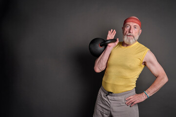 athletic senior man is training with a heavy iron kettlebell, fitness over 60 concept