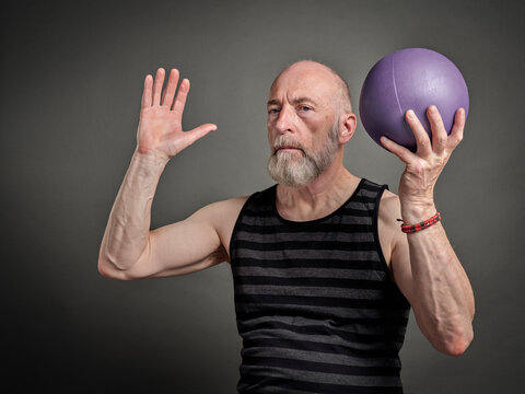athletic senior man (late 60s) is exercising with a small medicine ball