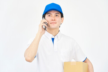段ボール箱を持ってスマホで話すキャップとポロシャツのユニフォームの男性　白背景