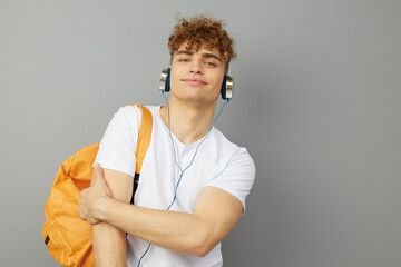 a curly-haired guy, a student, stands on a light background in a white cotton T-shirt and hugs himself while listening to music with headphones