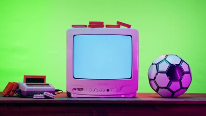 Old television with grey interference screen on green neon background. Close-up of vintage tv and cartridges for retro playstation. Antique video game, and football ball, nostalgia.  - Powered by Adobe