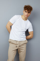 a relaxed, handsome man with curly hair stands on a gray background in a casual white T-shirt, looking pleasantly at the camera. Studio photography