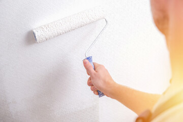 A man is painting vinyl wallpaper with a velour roller for painting with white paint. Renovation of the room.