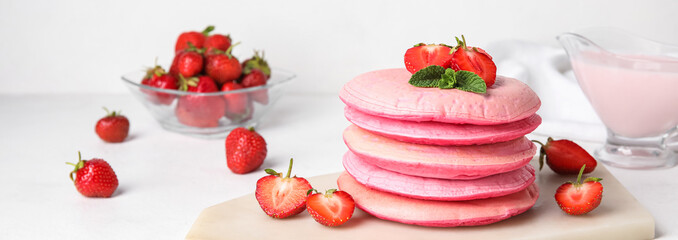 Tasty pink pancakes with strawberry on light background