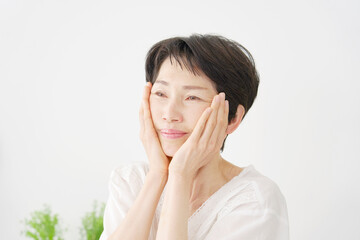 リビングでフェイシャルケアをする中年女性