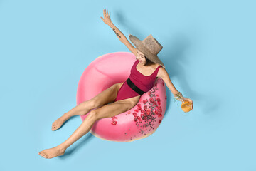 Beautiful happy young woman in swimsuit and with big tasty donut drinking cocktail on light blue...