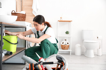 Asian female plumber fixing sink in bathroom