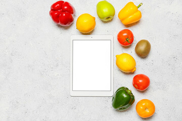 Tablet computer and different fruits, vegetables on light background. World Vegan Day concept