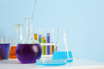 Different laboratory glassware with samples on table near blue wall