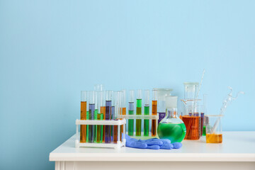 Different laboratory glassware with samples on table near blue wall