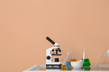 Modern microscope and laboratory glassware with liquid on table near beige wall