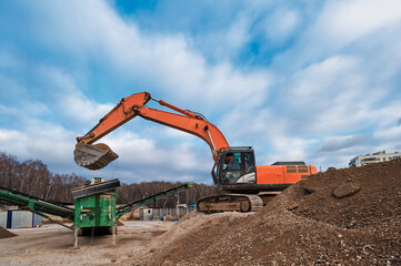 A construction excavator loads crushed stone into the receiving hopper of a mobile crushing and sorting complex.