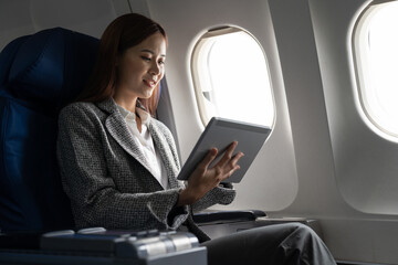 Travel and technology. Young asian woman in plane using digital tablet while sitting in airplane...