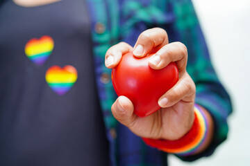 Asian woman holding red hert with rainbow flag, LGBT symbol rights and gender equality, LGBT Pride Month in June.