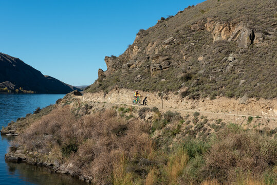 Cyclist on Lake Dunstan bike trail as it follows the lake shore. Otago, South Island, New Zealand.