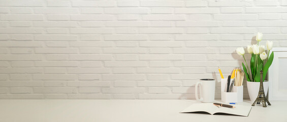 Minimal workplace with potted plant, pencil holder and books on white table against brick wall....