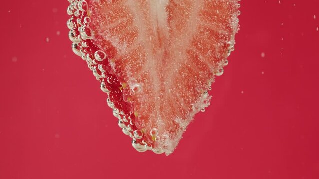 Strawberry in carbonated water. Cooking sweet cocktail, fizzy summer drink, cold lemonade with red berries, ripe fruits on red background.