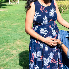 Indian couple posing for maternity baby shoot. The couple is posing in a lawn with green grass and the woman is falunting her baby bump in Lodhi Garden in New Delhi, India