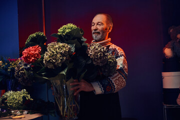 Portrait of modern flower market and elderly man florist with bouquet dressed in apron.