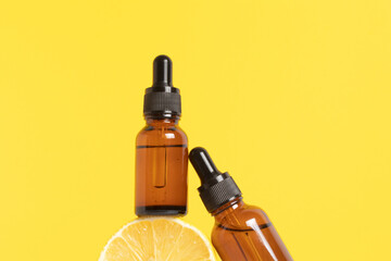 Serum with vitamin C. Lemon essential oil. Glass bottle with a pipette, half a lemon on yellow...