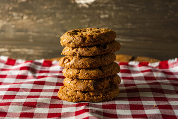 few homemade cookies with chocolate drops, stacked over each other, on red cloth table and wooden background. warm morning breakfast concept