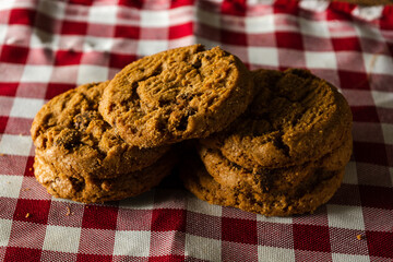 few homemade cookies with chocolate drops, stacked over each other, on red cloth table and wooden background. warm morning breakfast concept