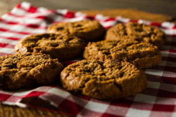 few homemade cookies with chocolate drops, stacked over each other, on red cloth table and wooden background. warm morning breakfast concept